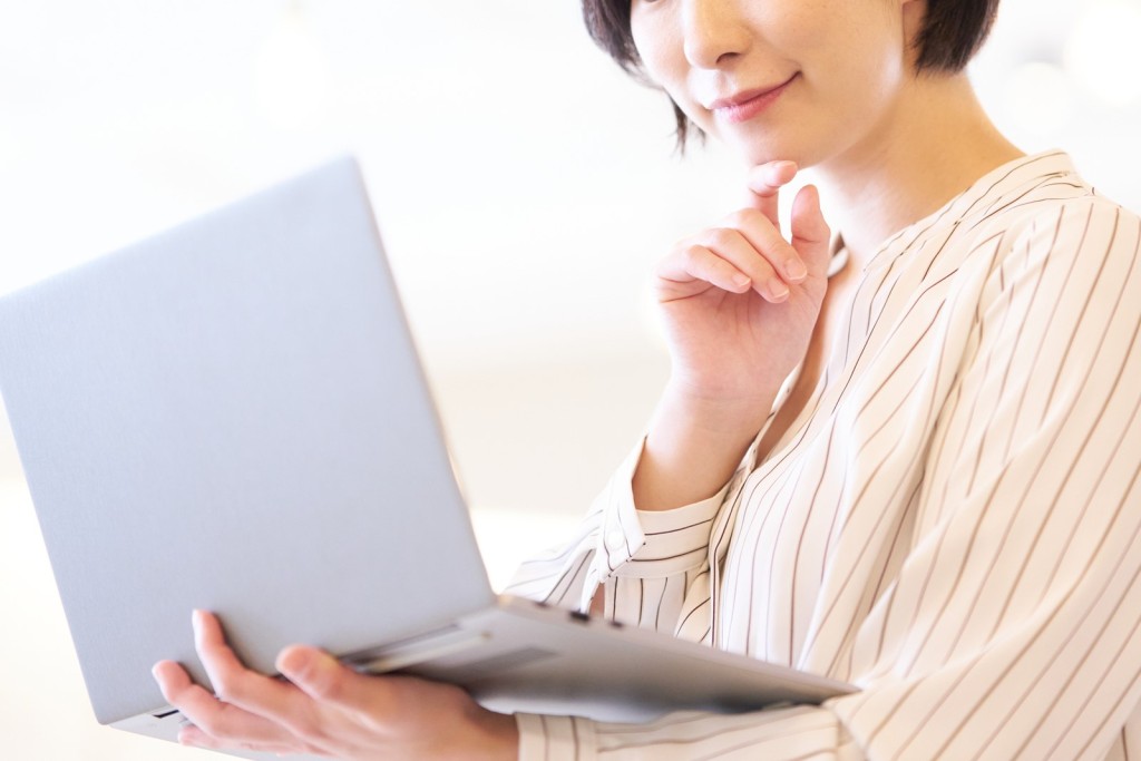 ノートパソコンを持ちながら思案する女性