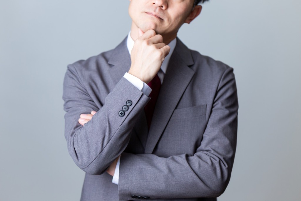 腕を組み考え込むスーツ姿の男性ビジネスパーソン