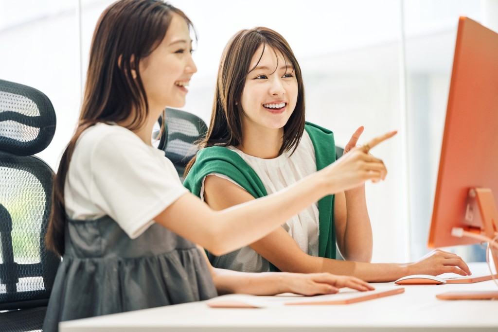 パソコン画面を見ながら笑顔で業務の確認をする2人の女性社員