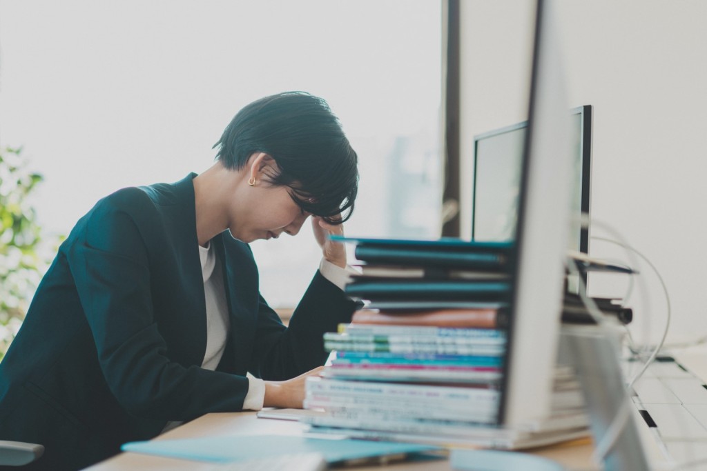 大量の書類やPCの前で頭を抱える女性