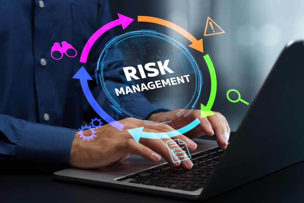 青いシャツを着た人物がパソコンを操作する手元と、RISK MANAGEMENTの文字を中心に双眼鏡・警告・虫眼鏡などのアイコンが円状に並んだグラフィック