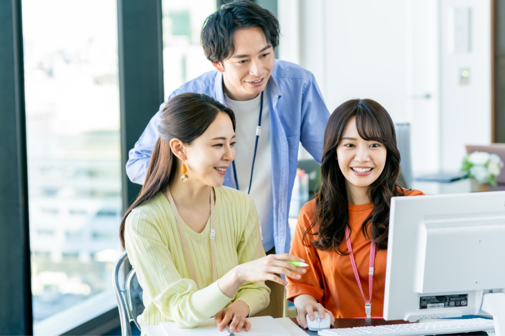 パソコン画面を見ながら笑顔で会話するオフィスワーカーたち