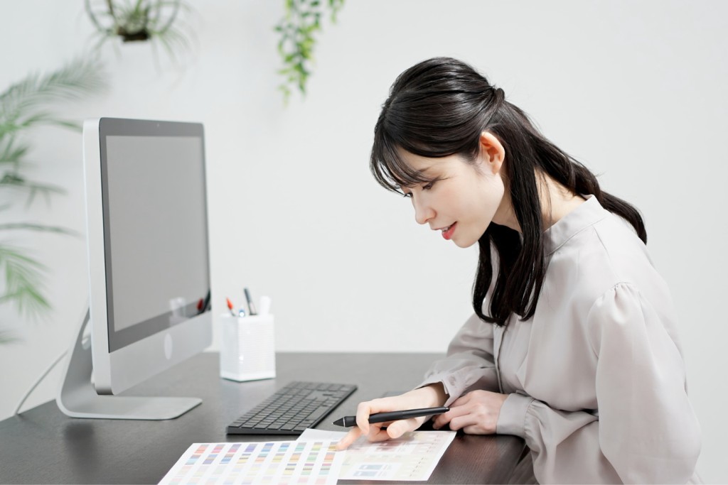 デスクトップパソコンの前で資料やペンを使い作業する女性