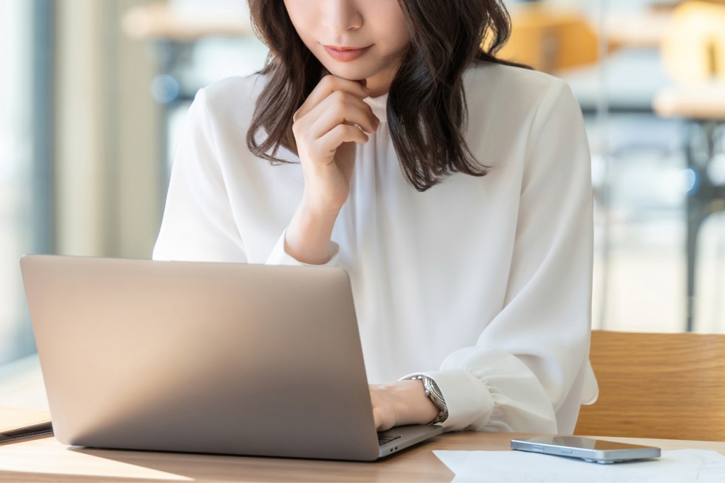 ノートパソコンの前で考え込む女性
