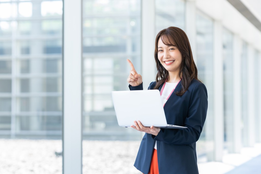 ノートパソコンを持って指差す笑顔の女性社員