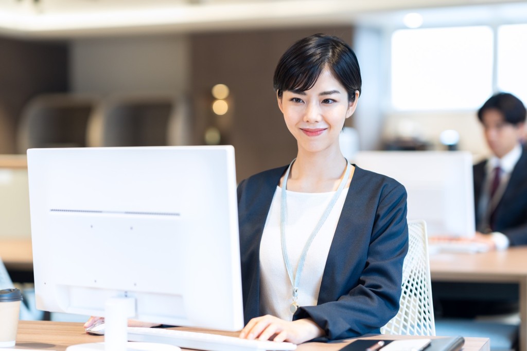 パソコンに向かって笑顔で作業するオフィスの女性社員